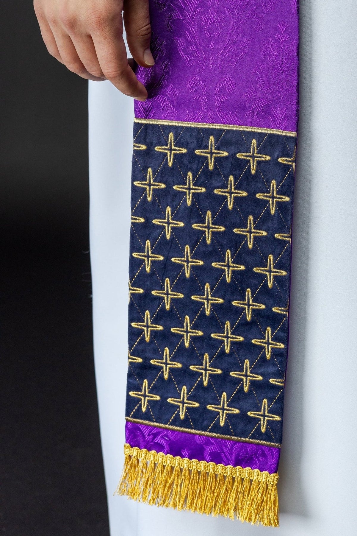 Stole detail showing purple jacquard fabric, navy panel with gold cross embroidery and gold fringe