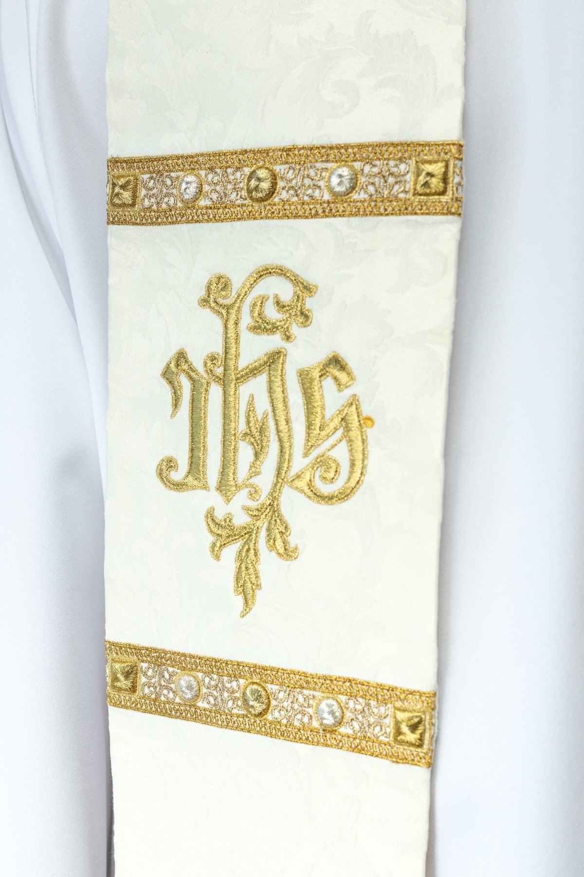 Ecru stole detail with gold embroidery and decorative bands showing the IHS motif
