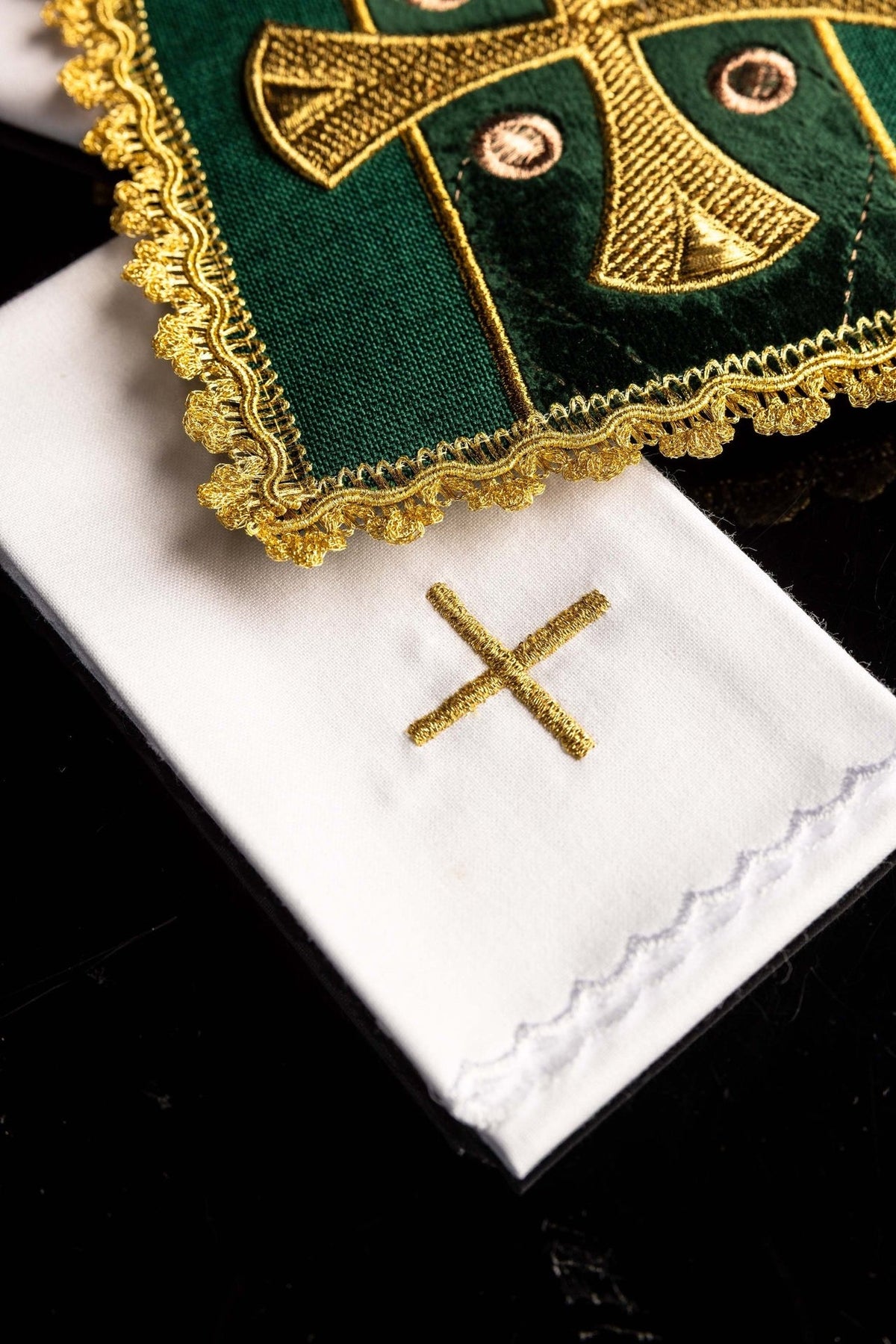 Green velvet pall close-up showing gold embroidery, ornate trim, and white linen beneath