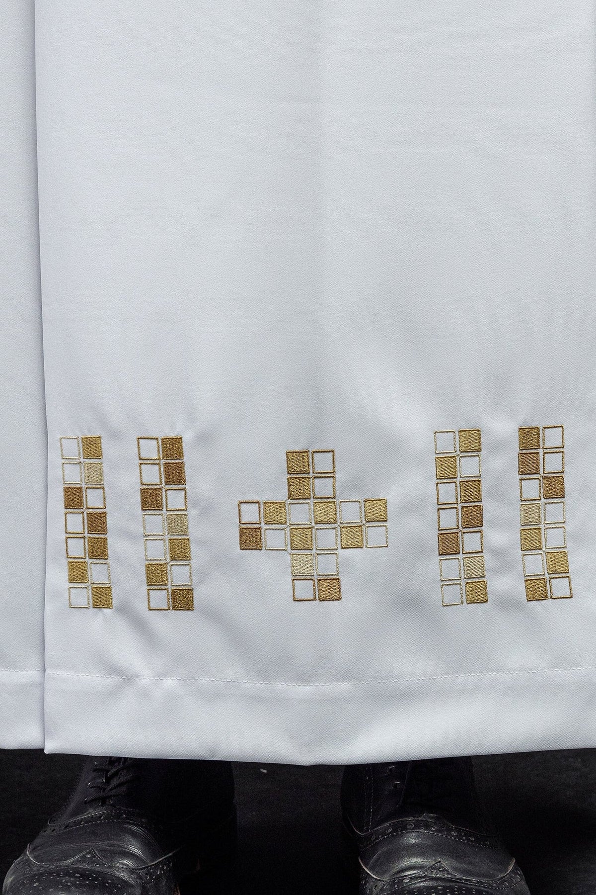 White alb close-up showing gold embroidered mosaic crosses along the hem