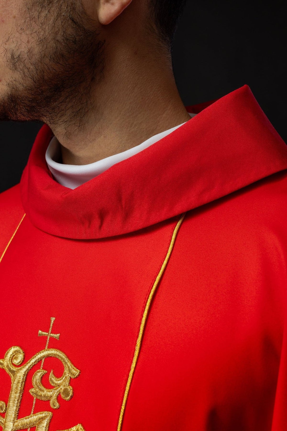 Red chasuble detail showing gold IHS embroidery and trimmed sleeve