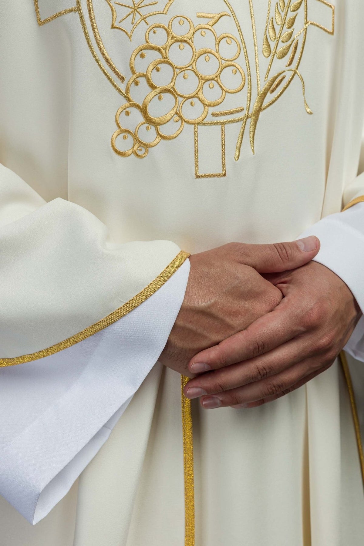 Ecru chasuble close-up showing embroidered gold cross, grapes and wheat motifs