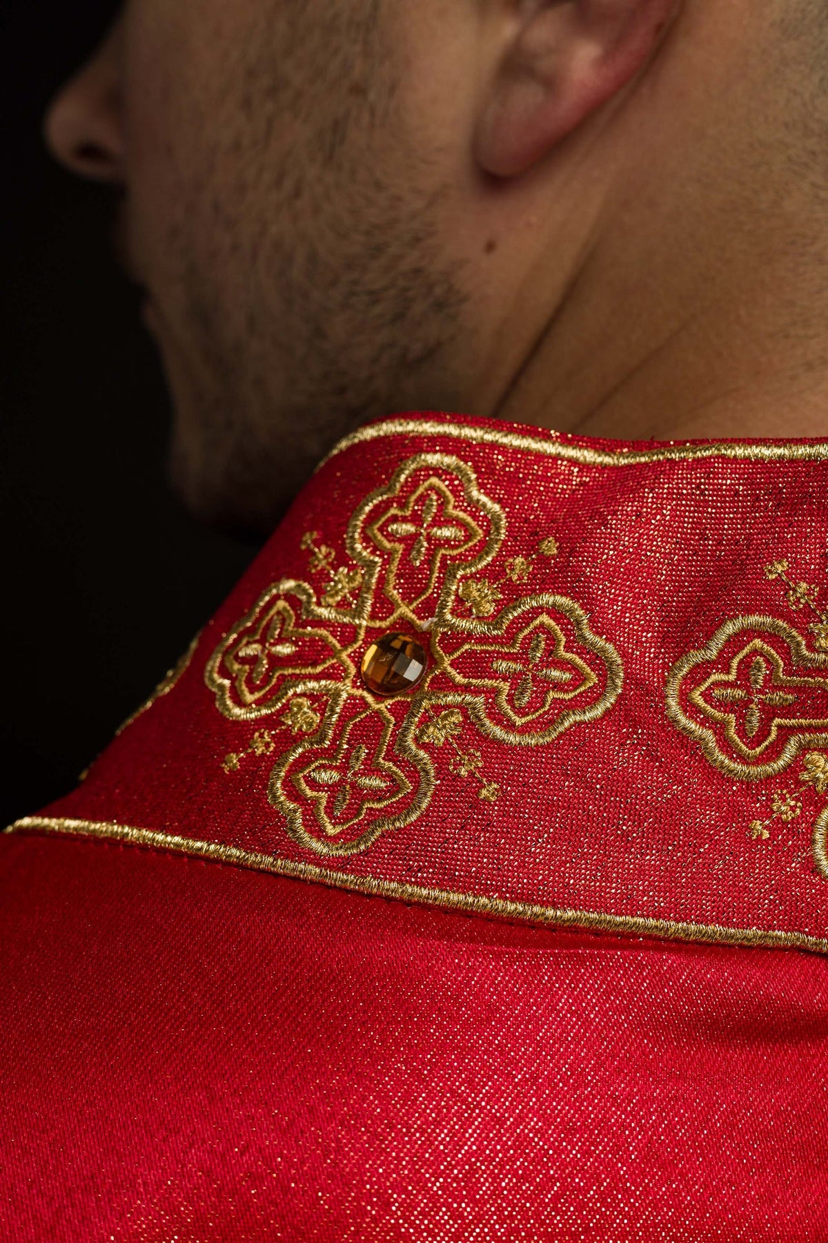 Red chasuble close-up showing stone-set collar and gold cross embroidery