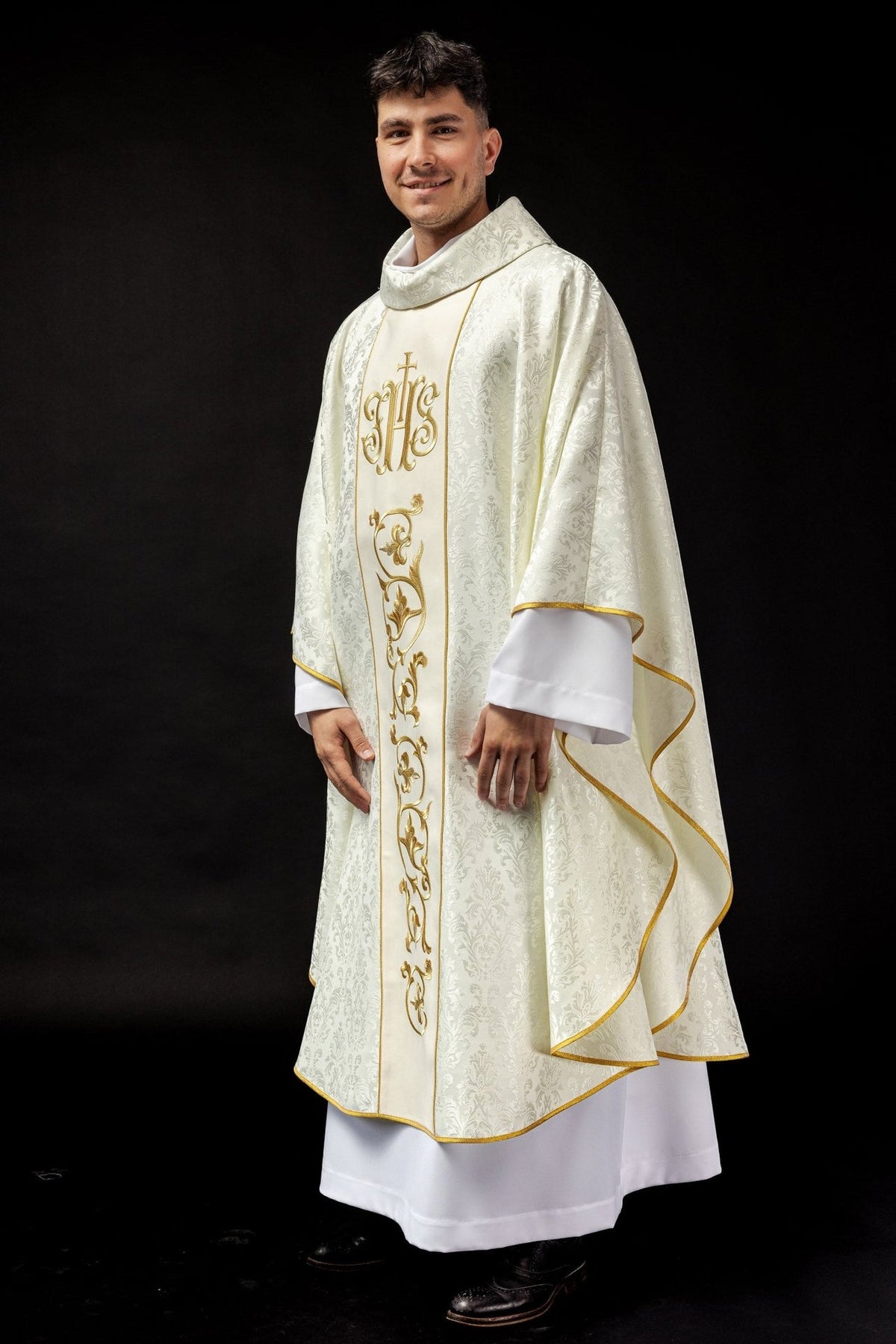 Ecru chasuble worn from the side, with gold IHS orphrey and wide flowing sleeves
