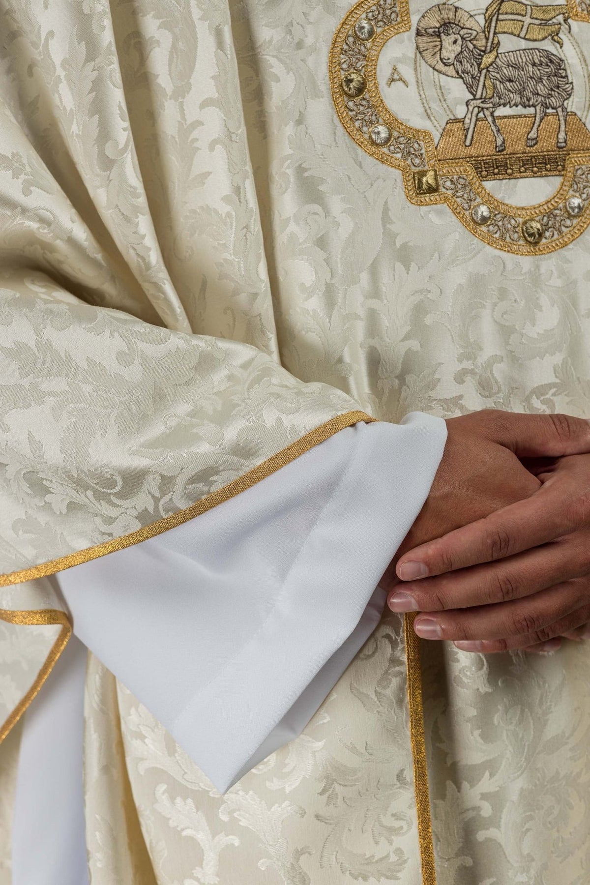 Ecru chasuble close-up showing jacquard floral fabric and gold-trimmed edge