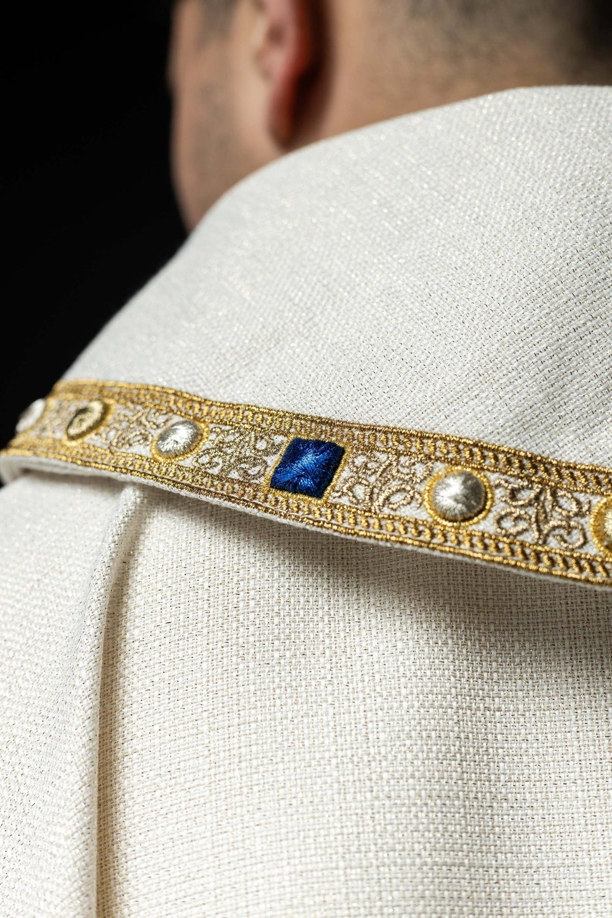 White chasuble sleeve close-up with gold edging and woven fabric