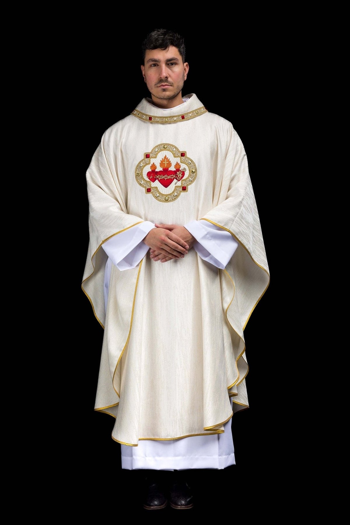 White chasuble worn full length, showing gold trim and three Sacred Hearts embroidery