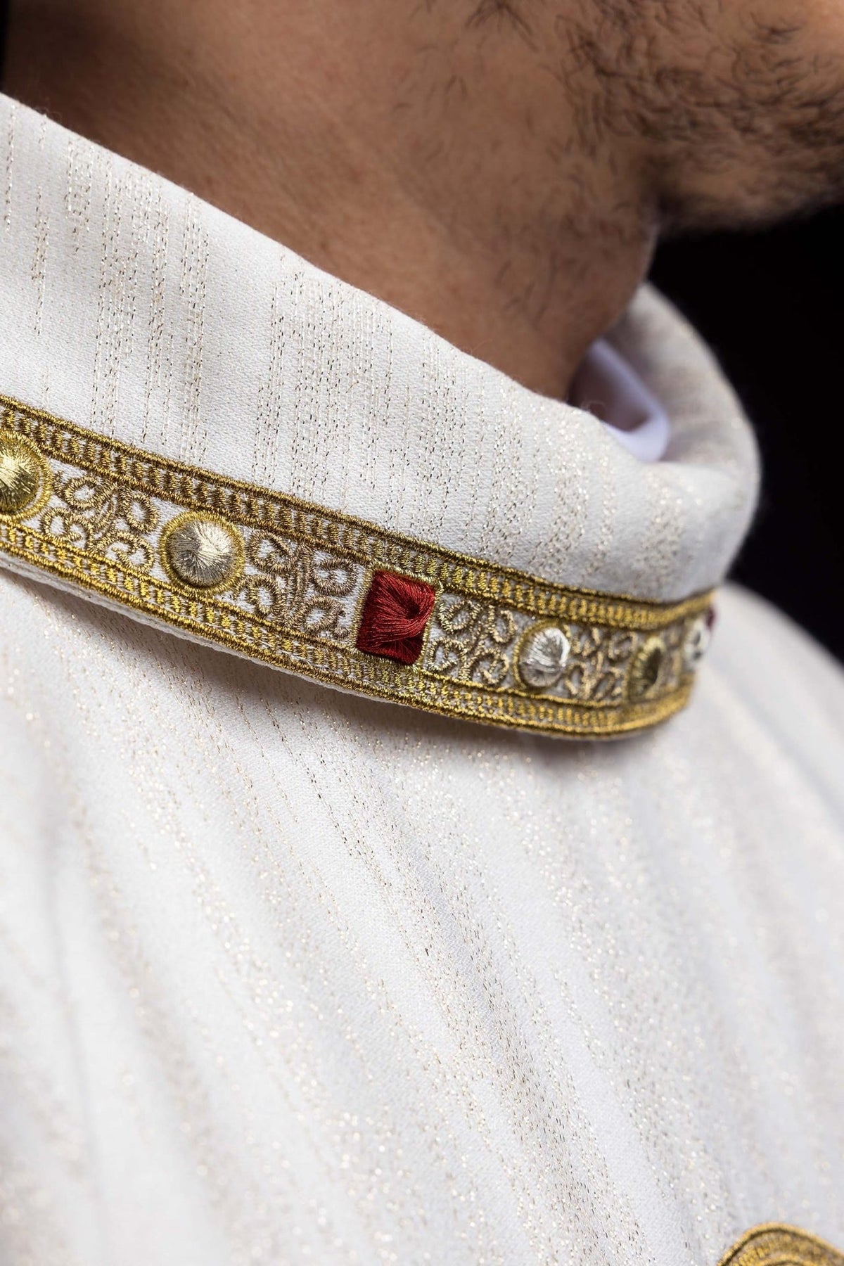 Chasuble close-up showing white fabric and ornate gold trim around the stand-up collar
