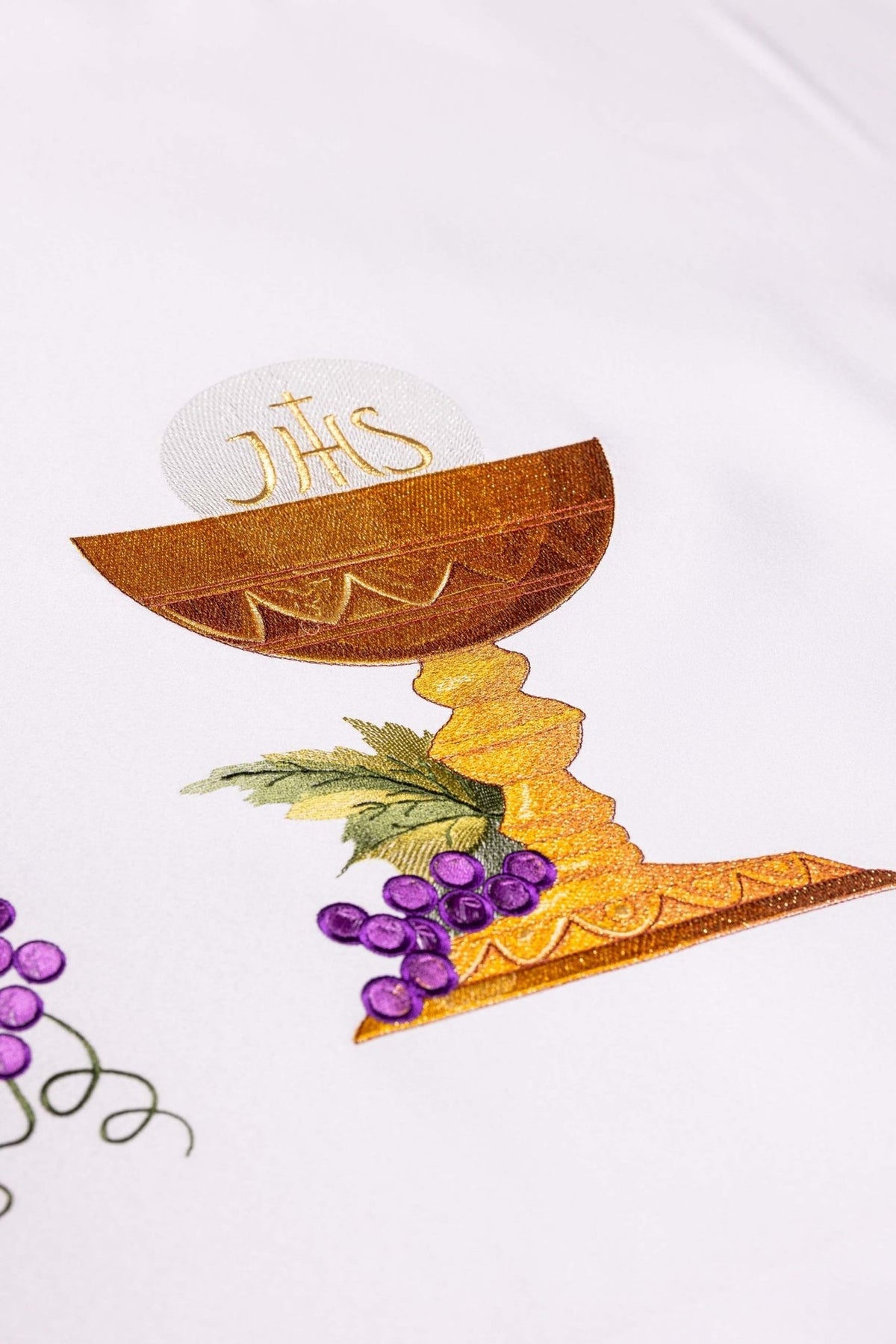 Altar cloth close-up showing embroidered gold chalice, white host with IHS monogram, and purple grapes