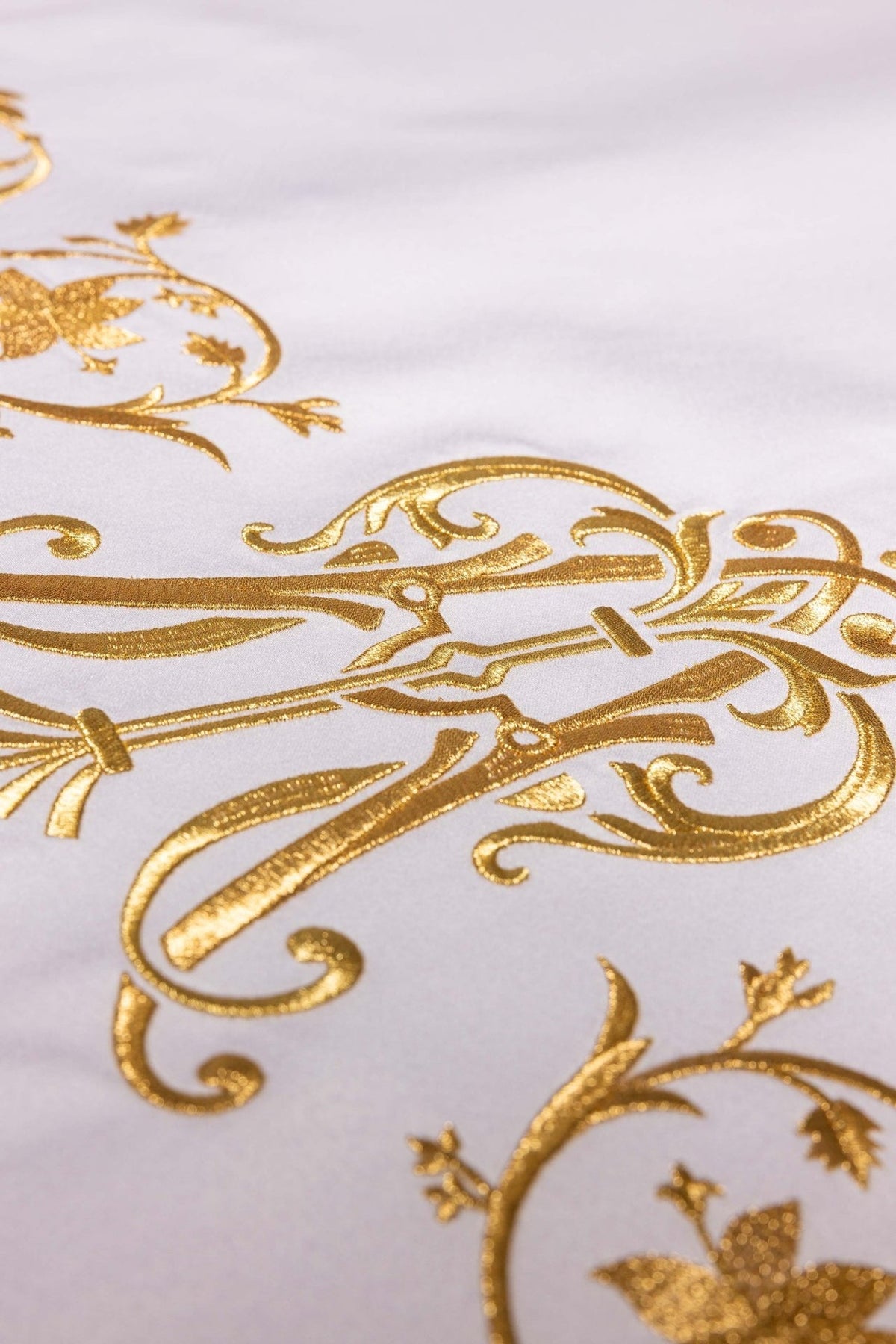 Altar cloth detail showing gold floral embroidery beside the Marian symbol