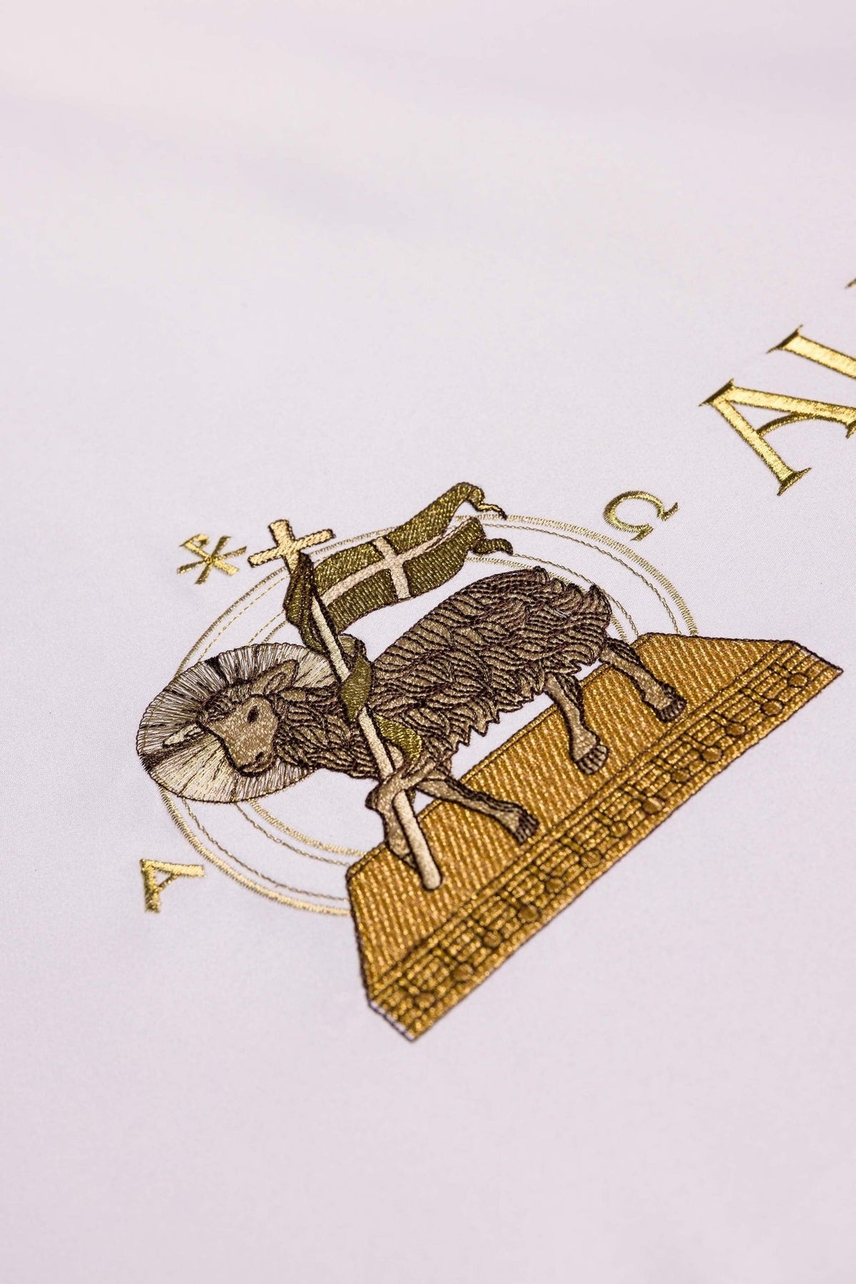 Altar cloth close-up showing gold Agnus Dei embroidery with cross and banner