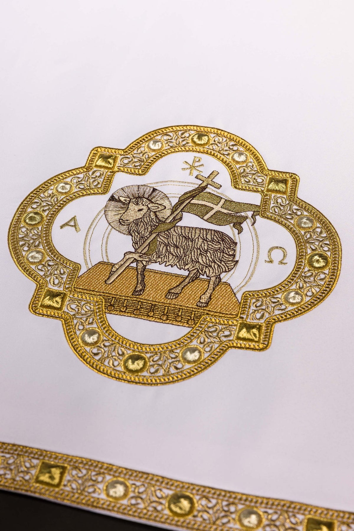 Altar cloth detail showing ornate gold-framed Agnus Dei embroidery and border