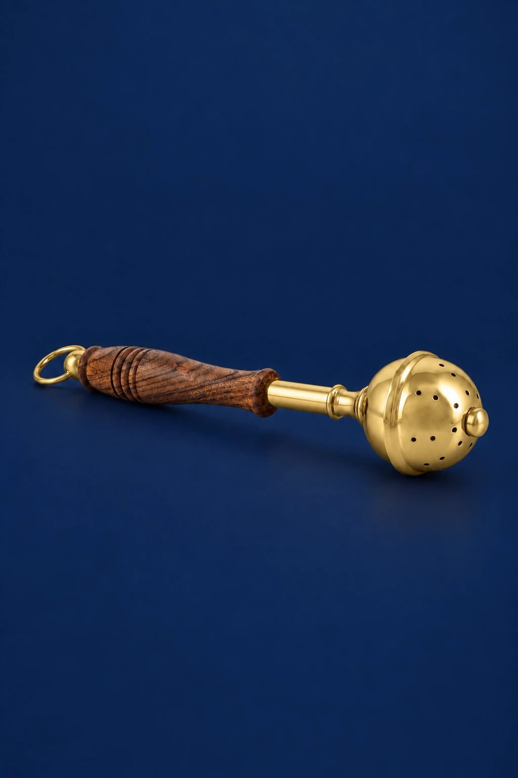 Side view of a brass aspergillum with a carved wooden handle and hanging ring