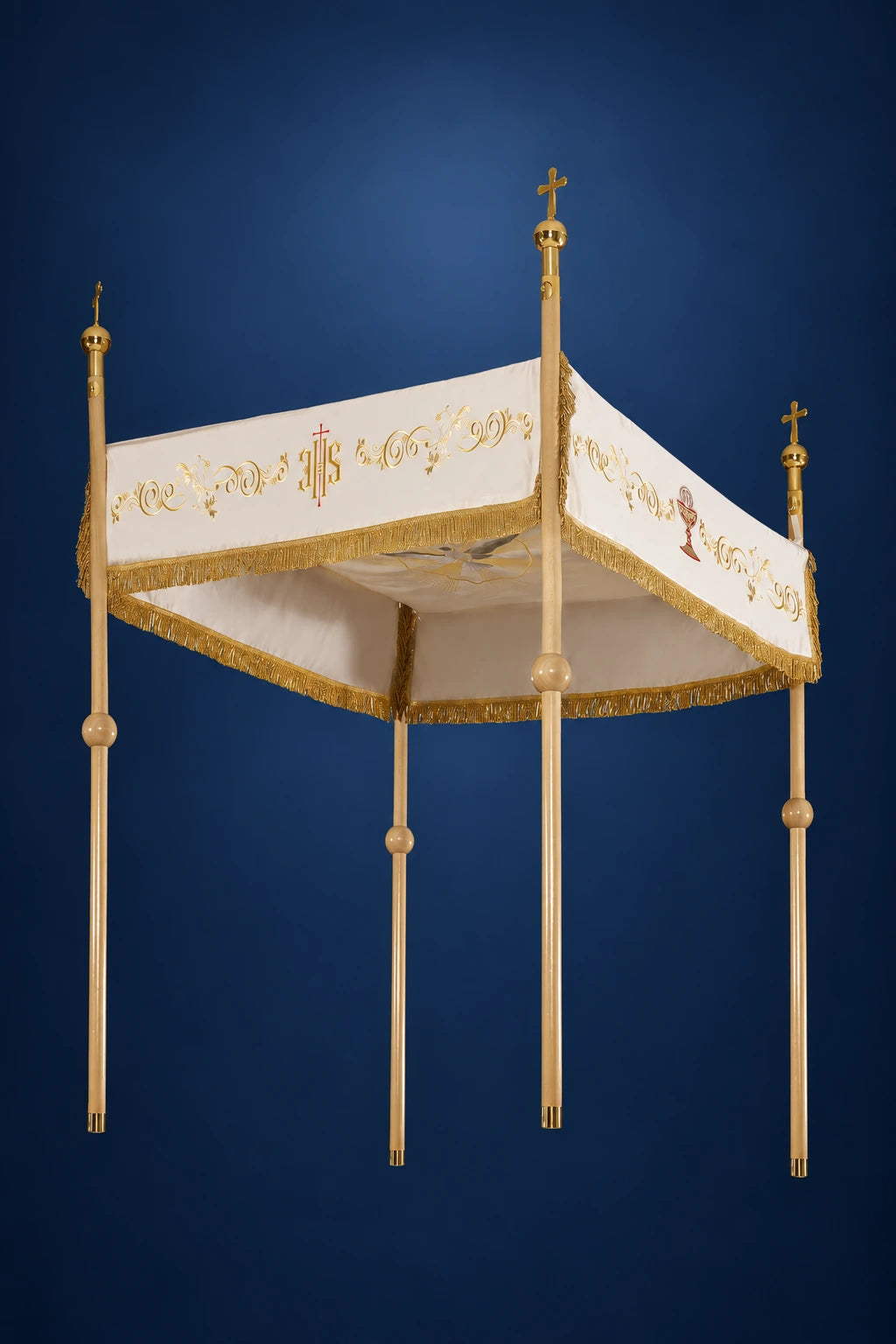 Three-quarter view of an ecru processional canopy with gold fringe, IHS motif, and four carrying poles