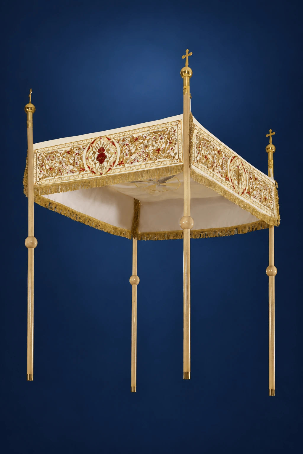 Three-quarter view of an embroidered ecru processional canopy with gold trim, fringe, and four tall support poles