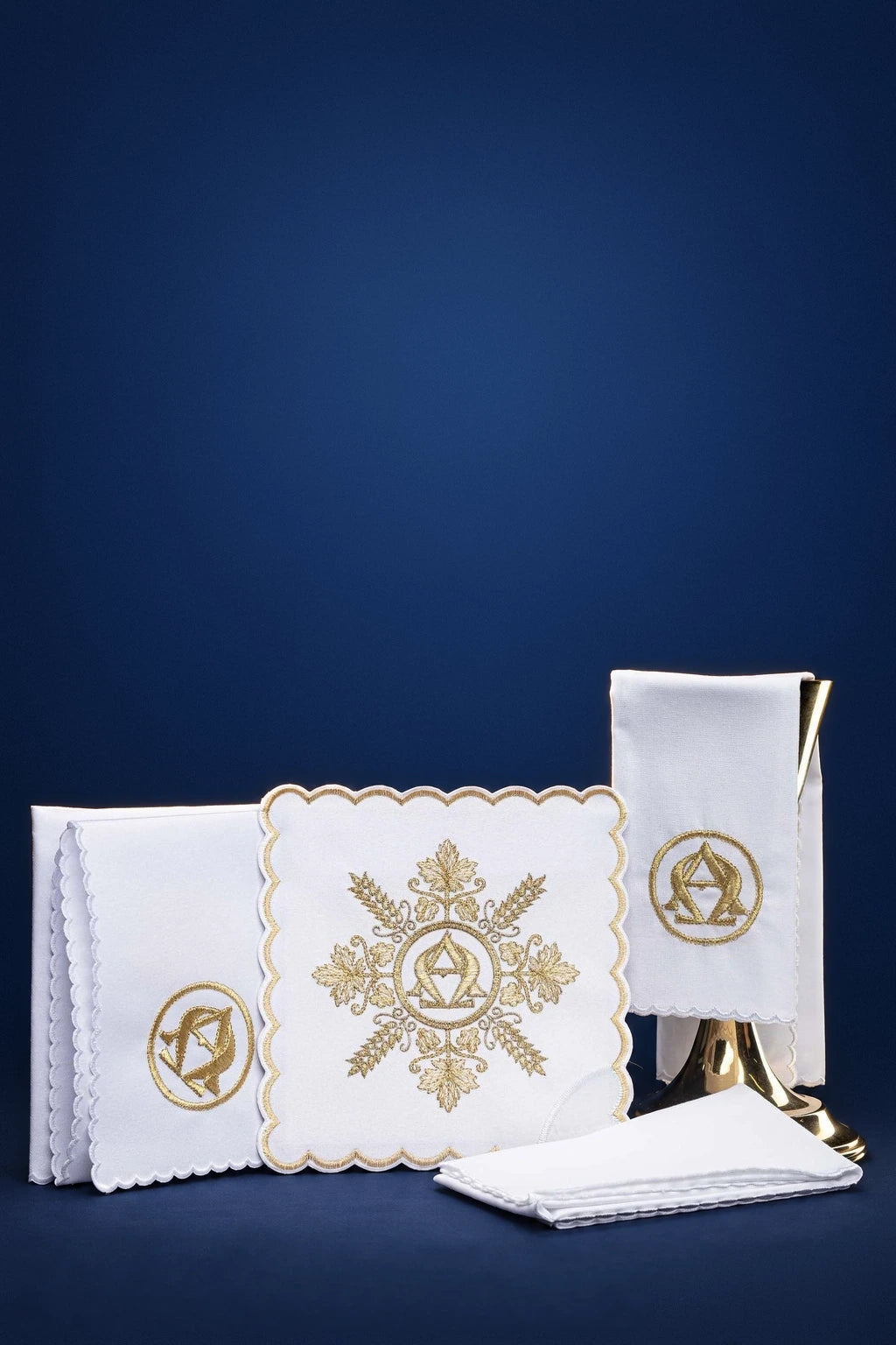 White altar linen set with gold Alpha Omega embroidery, shown folded with a scalloped embroidered cloth and matching