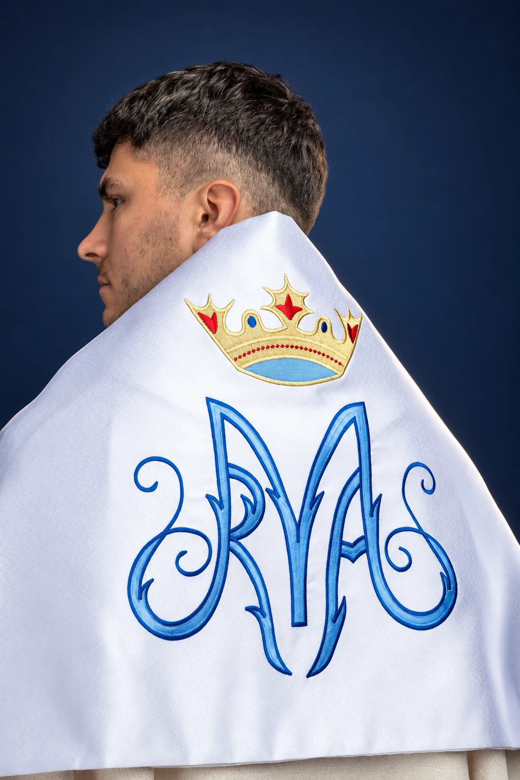White humeral veil draped over the shoulders, shown from the back, with embroidered Marian symbol and crown motif